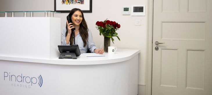 Receptionist at Pindrop Hearing smiling on the phone behind her desk